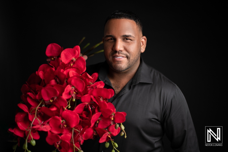 A Man Holds a Striking Bouquet of Red Orchids in a Studio Setting, Showcasing a Confident Smile Against a Dark Background During a Portrait Session