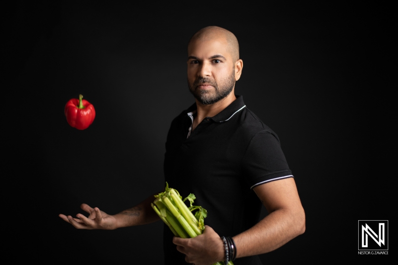 A Man Skillfully Juggling a Red Bell Pepper While Holding a Bunch of Celery Against a Dark Background, Showcasing a Blend of Culinary Creativity and Performance Art