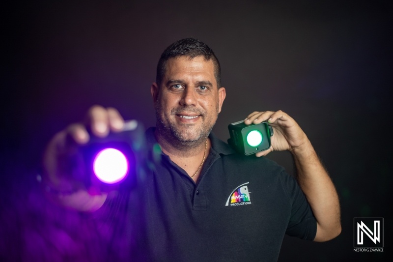 A Man Holds Multicolored Stage Lights While Smiling, Showcasing His Passion for Lighting Design in a Studio With a Dark Background