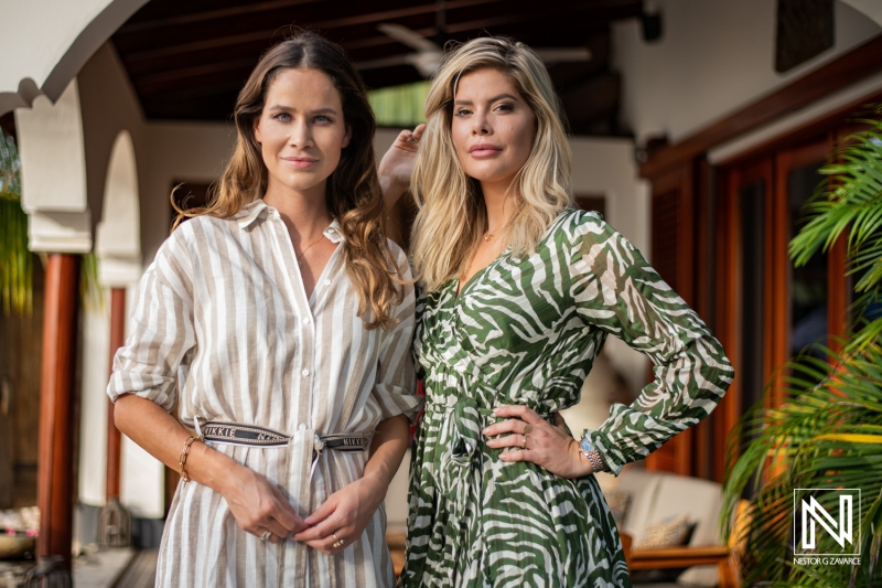 Two Women Posed Confidently in Stylish Outfits Against a Backdrop of Palm Trees and Elegant Architecture During a Sunny Outdoor Gathering