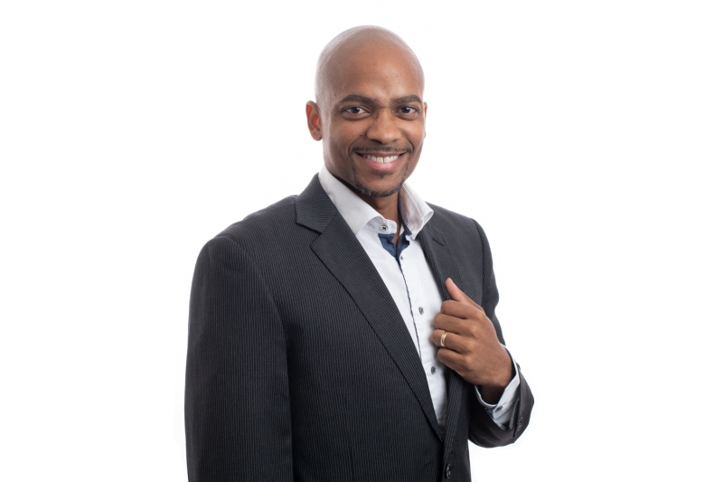 A Smiling Man in a Professional Suit Stands Confidently Against a White Background, Highlighting His Approachable Demeanor and Readiness for a Business Meeting