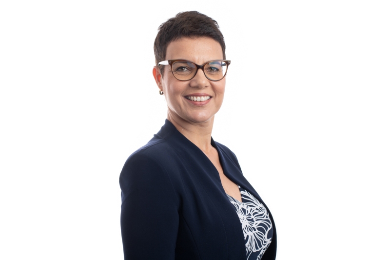 Professional Woman With Glasses Poses Confidently Against a Plain Background, Showcasing Her Attire and Friendly Demeanor in a Studio Setting