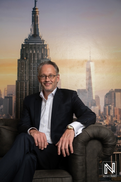 A Professional Portrait of a Man Seated on a Couch With the New York City Skyline in the Background During Sunset, Highlighting Iconic Skyscrapers