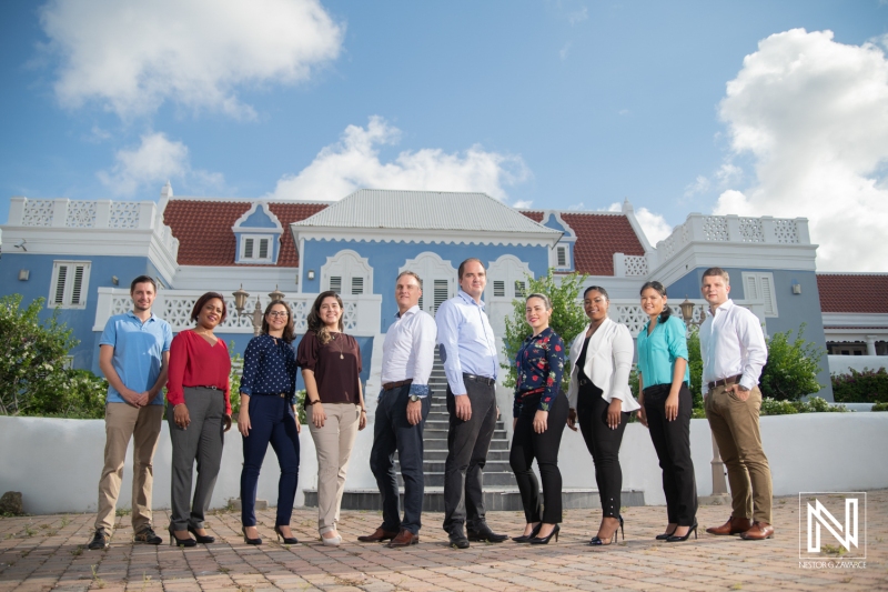 A Group of Diverse Professionals Poses for a Photo in Front of a Historic Blue Building in the Caribbean During a Sunny Day, Showcasing Unity and Collaboration