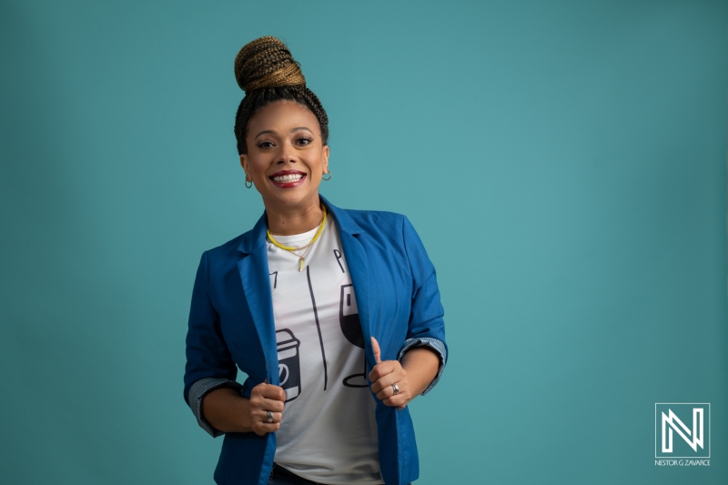 A Woman With Braids Poses Confidently in a Blue Blazer and Graphic Tee Against a Turquoise Backdrop, Smiling Cheerfully and Showcasing Her Style