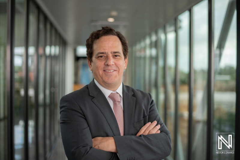 A Smiling Professional Man in a Business Suit Stands Confidently With Crossed Arms in a Modern Office Corridor During Daytime, Reflecting a Successful Work Environment