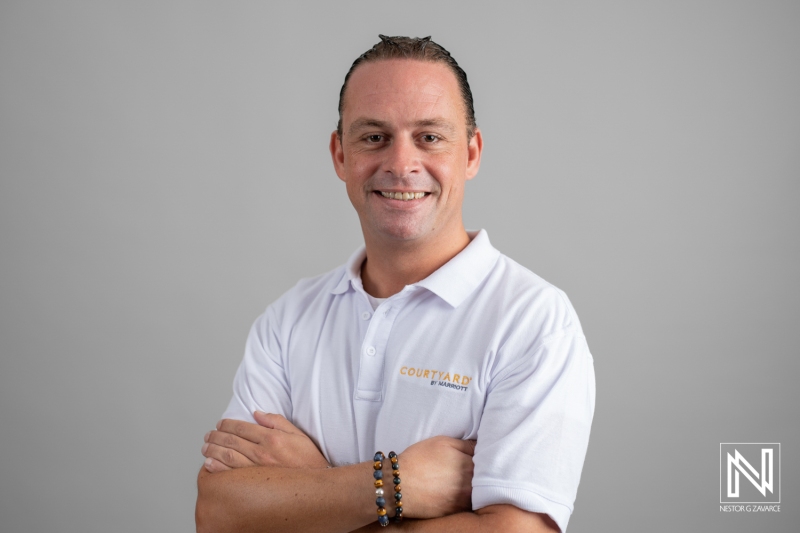 A Professional Man in a White Collared Shirt Stands Confidently Against a Neutral Gray Background, Showcasing a Friendly Smile and Crossed Arms While Exuding Approachability