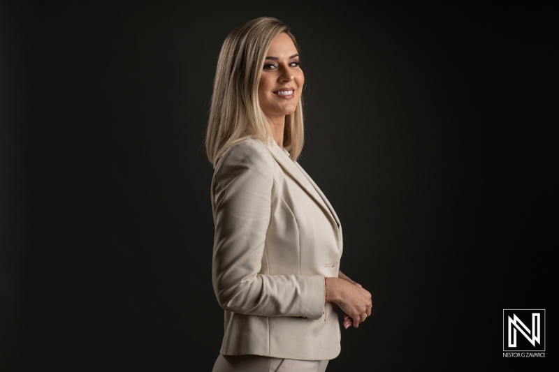 Confident Woman in a Light-Colored Tailored Suit Poses Elegantly Against a Dark Backdrop, Showcasing Her Professional Demeanor During a Studio Shoot