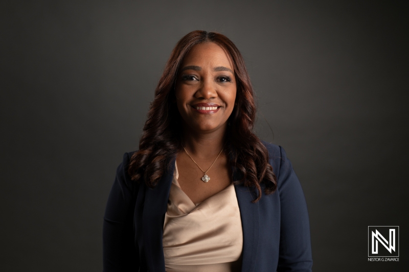 A Confident Woman in Business Attire Smiles Warmly While Standing Against a Dark Background, Showcasing Professionalism and Approachability During a Studio Portrait Session