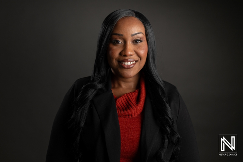 A Smiling Woman With Long Black Hair Wearing a Red Sweater and Black Jacket Poses Confidently Against a Dark Background, Exuding Warmth and Professionalism