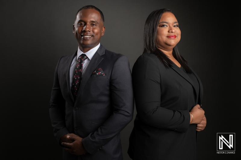 Professional Couple in Business Attire Poses Confidently Against a Dark Backdrop, Showcasing Unity and Success in Their Careers During an Elegant Photoshoot