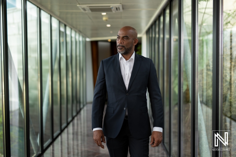 A Well-Dressed Man Confidently Walking Through a Modern Glass Corridor in an Upscale Building During Daylight Hours