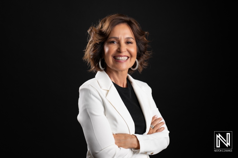 A Confident Businesswoman Stands With Arms Crossed, Smiling Brightly Against a Dark Backdrop, Conveying Positive Energy During a Professional Photoshoot