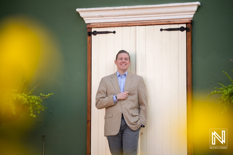 Corporate headshot taken in Curacao with a smiling person beside a door while yellow flowers are in view