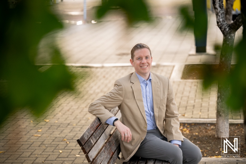 Corporate headshot taken in Curacao showing a man seated on a bench with a casual smile