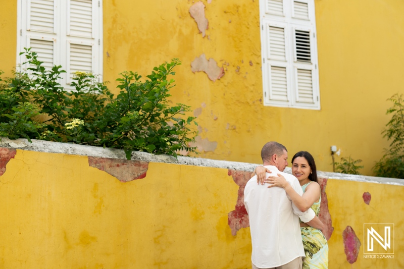 A Couple Joyfully Embraces in Front of a Vibrant Yellow Wall, Showcasing Love and Connection in a Picturesque Outdoor Setting