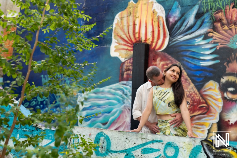 Couple Enjoying a Romantic Moment by a Vibrant Mural in an Urban Setting on a Sunny Day, Surrounded by Greenery and Colorful Street Art