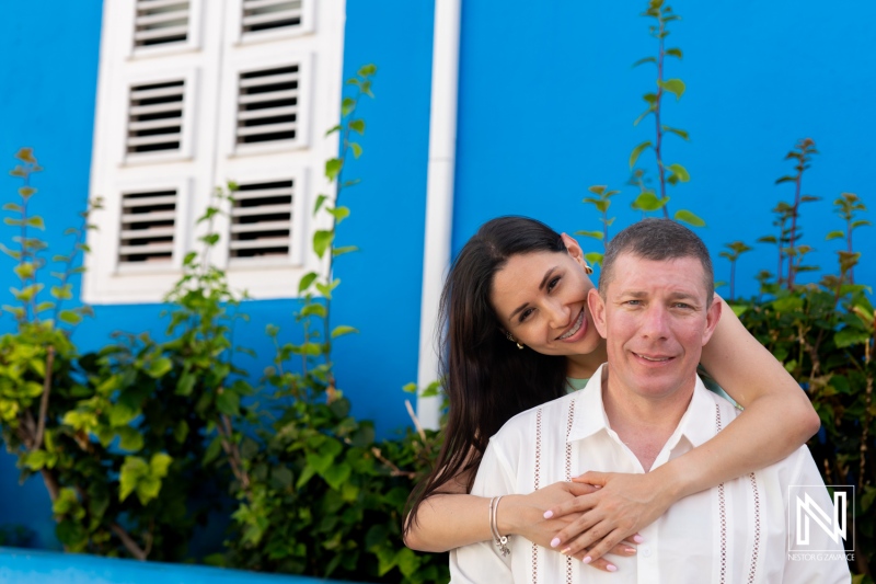 A Couple Enjoys a Joyful Moment Together by a Vibrant Blue Wall Adorned With Greenery in a Tropical Setting During a Sunny Day