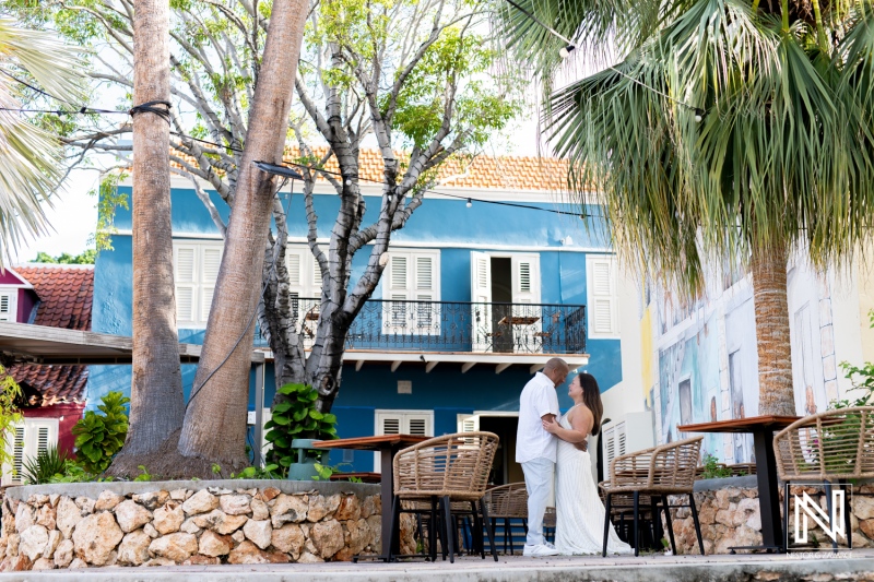 Couple shares a romantic moment in a charming courtyard in Curacao surrounded by tropical greenery and colorful buildings