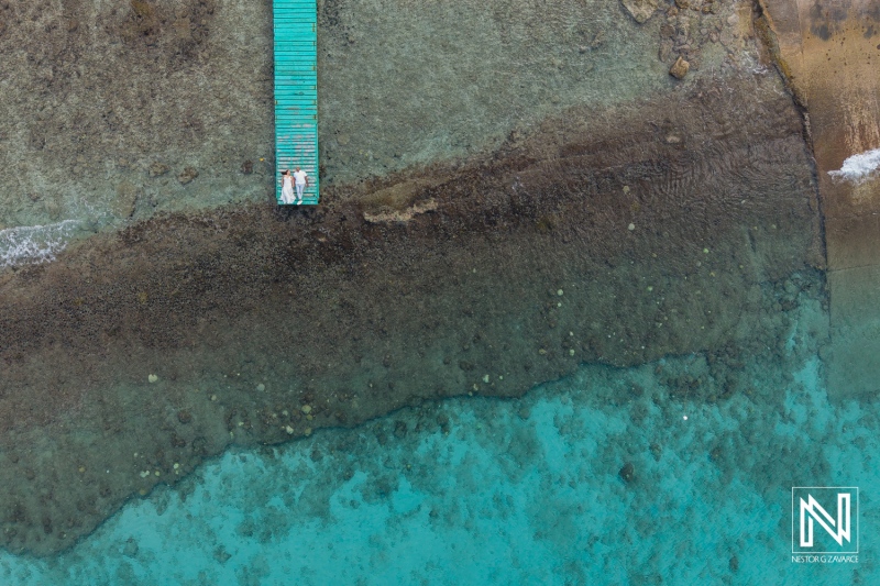 Couple enjoying a serene moment on a wooden dock in Curacao against a backdrop of clear turquoise waters and coral formations
