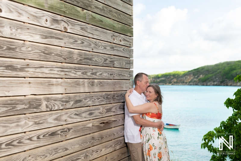 Couple Enjoying a Tender Moment by the Seaside as They Embrace Each Other Near a Rustic Wooden Structure During a Sunny Day