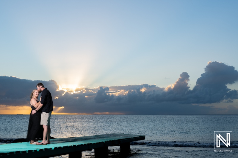 Couple enjoys a romantic sunset on a pier in Curacao, surrounded by stunning ocean views and dramatic clouds in the evening sky