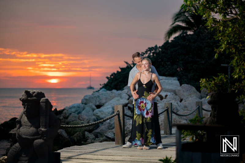 Couple enjoys a sunset photoshoot at Baoase Luxury Resort in Curacao while standing on a wooden path near the beach