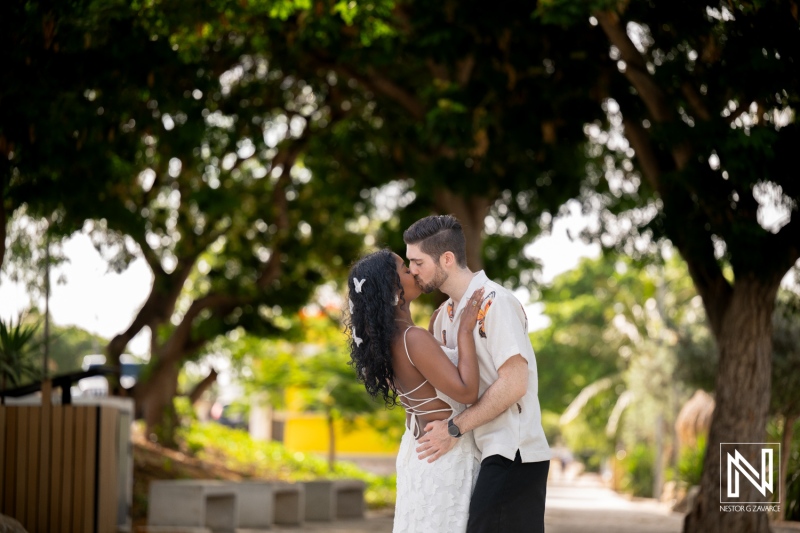 Couple shares a kiss during engagement session at Marie Pampoen in Curacao in the morning sunlight by the trees