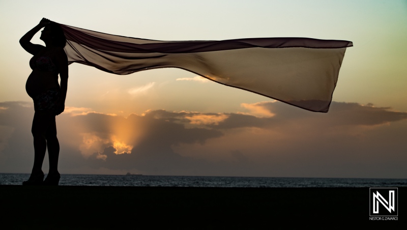 Expecting mother gracefully poses with flowing fabric against the stunning sunset in Curacao, capturing the beauty of pregnancy