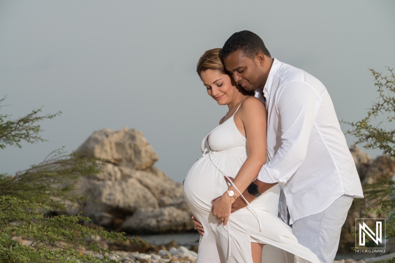 Maternity photoshoot capturing joy in Curacao with couple by the rocky coastline during sunset