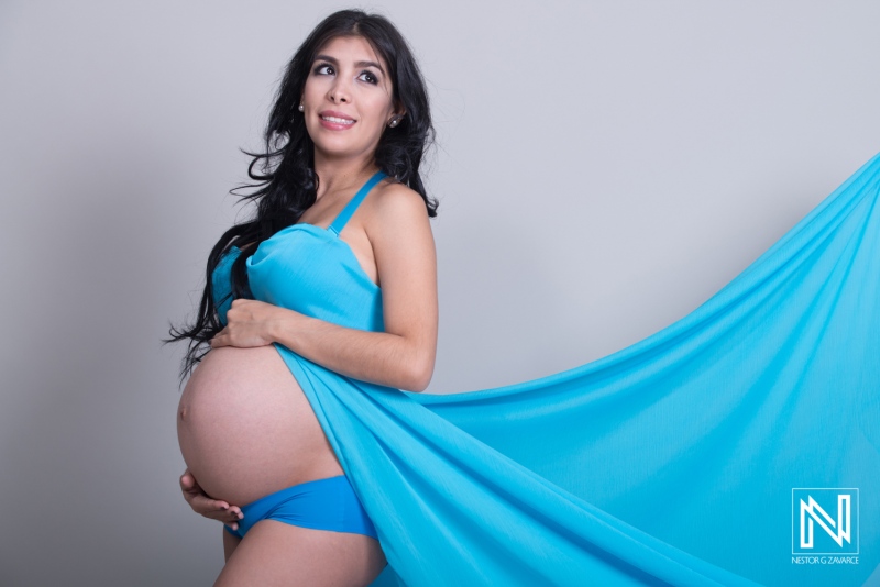 Beautiful maternity photoshoot in Curacao featuring a pregnant woman draped in blue fabric against a neutral background