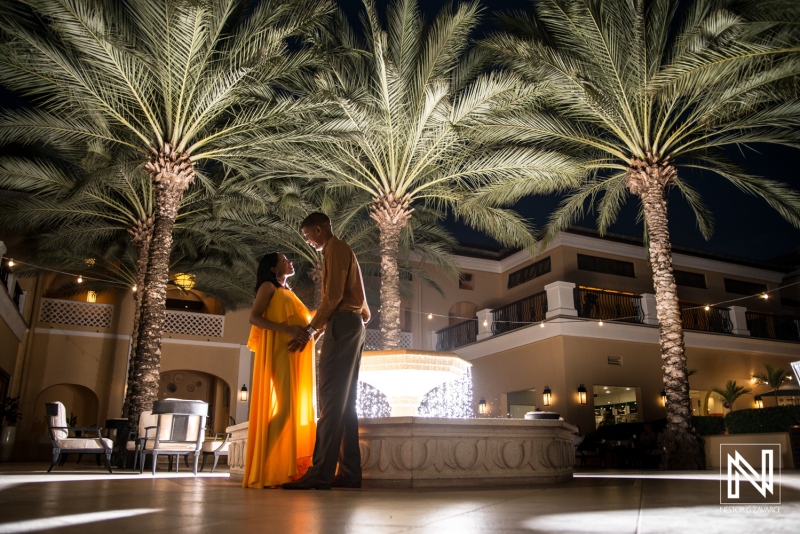 Expecting parents celebrate in a vibrant courtyard surrounded by palm trees in Curacao during a serene evening