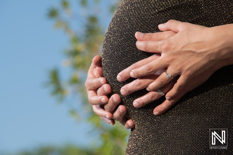 Hands gently cradling a pregnant belly under the sunny skies of Curacao in a serene maternity moment