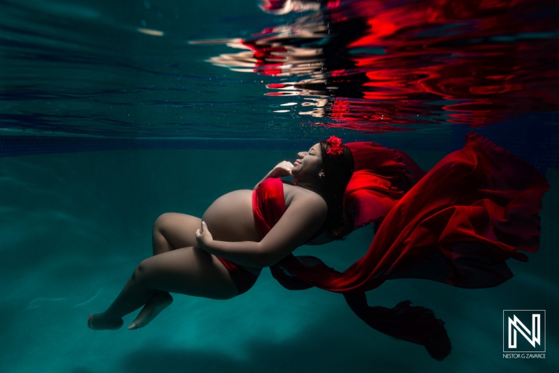 Expecting mother gracefully floating underwater in Curacao surrounded by vibrant fabric during a serene maternity photoshoot