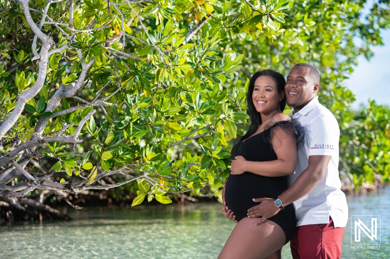 Expectant couple enjoying a serene moment by the water in Curacao surrounded by lush greenery during their maternity photoshoot