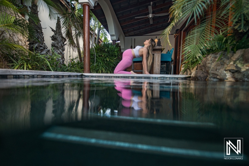 Expecting mother practices yoga by the pool in Curacao surrounded by lush greenery during sunset hours