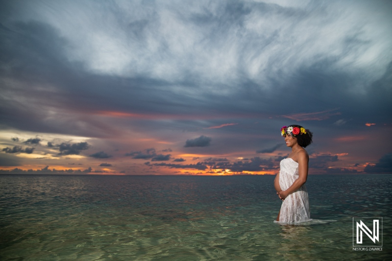 Maternity photo session during sunset in Curacao featuring a pregnant woman standing by the shore with a flower crown