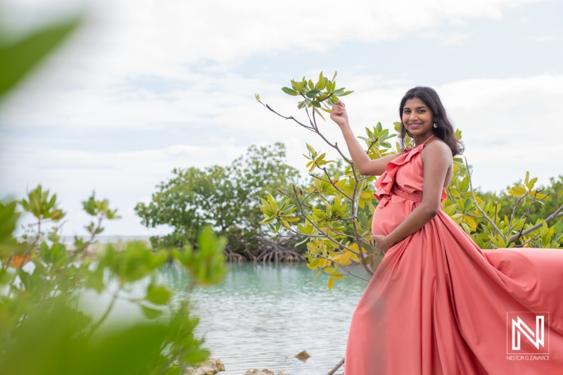 Expecting joy in Curacao with a serene backdrop near the water, a radiant maternity celebration in a flowing coral dress