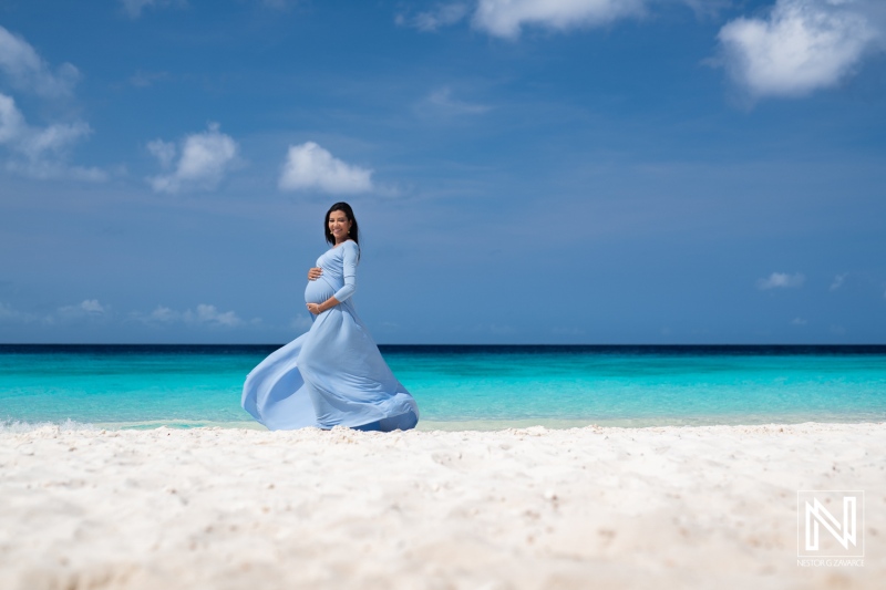 Maternity photoshoot on the beautiful beaches of Curacao showcasing a pregnant woman in a flowing blue dress by the turquoise waters