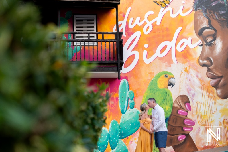 Maternity couple poses against colorful mural in Curacao, capturing joy of pregnancy and vibrant local art