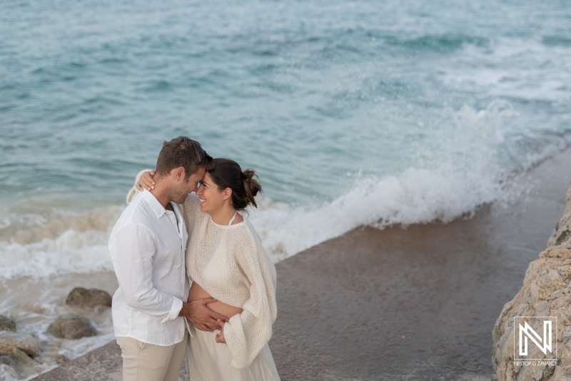 Maternity photoshoot capturing a couple embracing by the sea in Curacao during a beautiful sunset