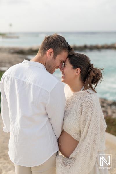 Expecting parents embrace in a maternity photoshoot on the shores of Curacao during a serene sunset