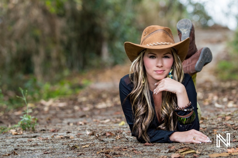 Young woman in a cowboy hat poses gracefully on a rugged path surrounded by nature during a sunny day