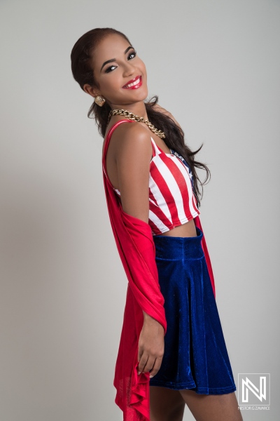 Young woman in stylish red and white striped top with blue skirt posing confidently against a plain background in a studio setting