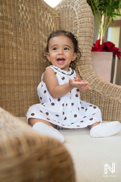 Happy toddler in a polka dot dress playing on a light beige cushion seat at a cozy indoor setting during daytime