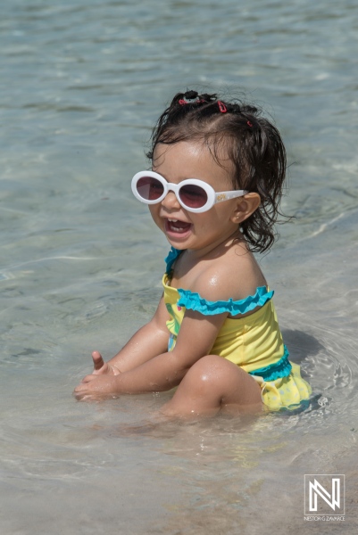 Young child enjoying a sunny day at the beach, playing in shallow water while wearing a colorful swimsuit and sunglasses