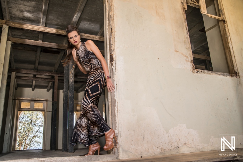 A model poses gracefully in a stylish patterned outfit near an open doorway of an abandoned building in bright daylight