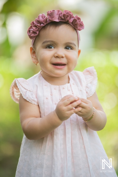 A joyful toddler with a flower headband smiling and playing outdoors in a sunny garden during a warm afternoon