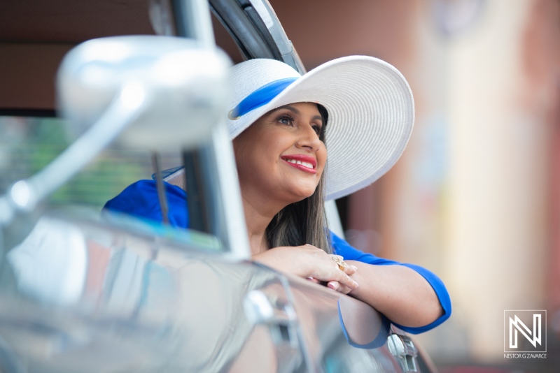 Woman wearing a stylish hat leans out of a car window while smiling during a sunny day in an urban setting, capturing a moment of joy and relaxation