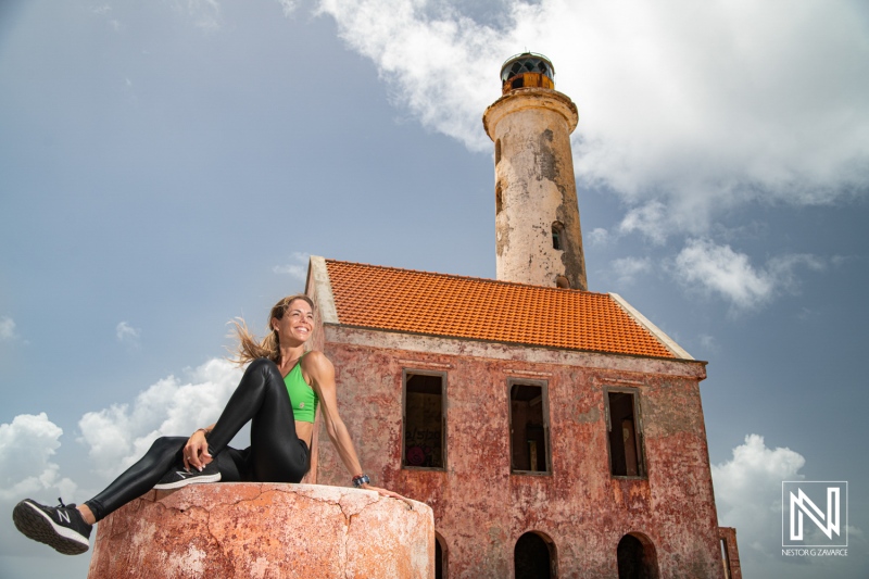 A young woman poses on a stone at an abandoned lighthouse in the Caribbean under a bright blue sky during daytime exploration